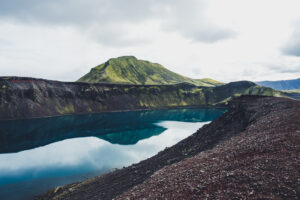 Modré kráterové jezero Hnausapollur obklopené tmavými vulkanickými svahy