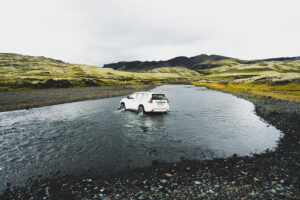 Bílé auto 4×4 při brodění řeky v islandských Highlands