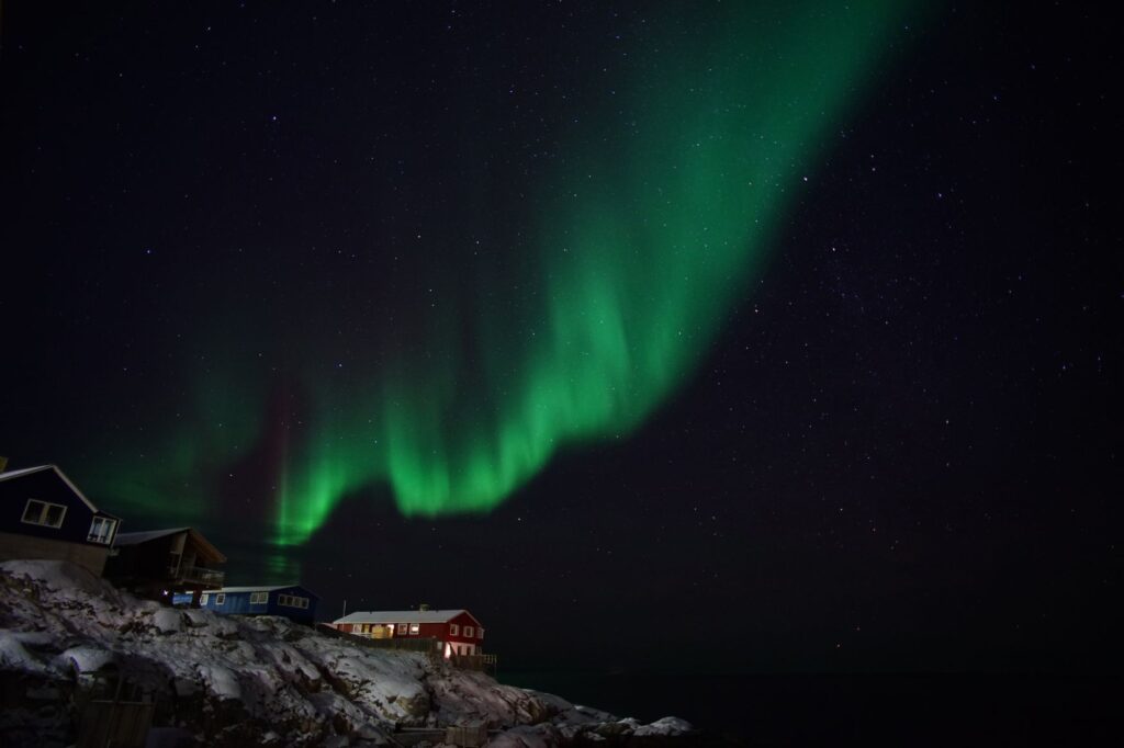 Zelená polární záře (aurora borealis) nad domy na pobřeží Ilulissatu v Grónsku