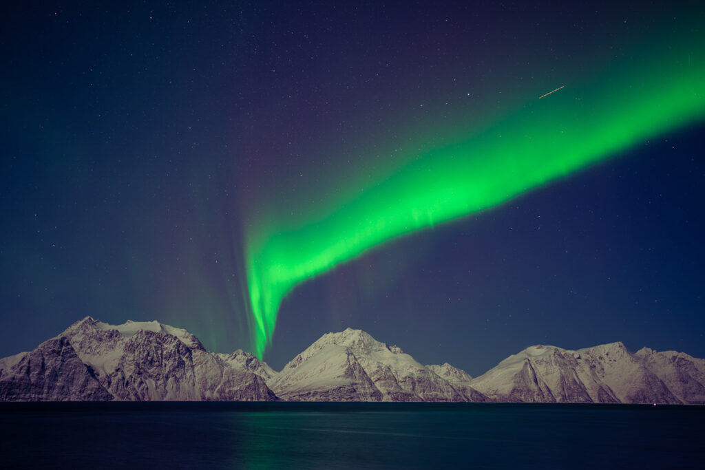 Zelená polární záře nad zasněženými Lyngenskými Alpami nedaleko Tromsø v Norsku