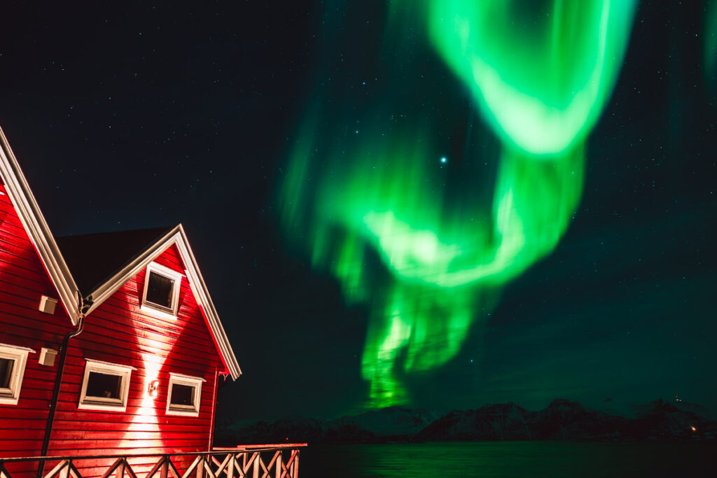 Zelená aurora borealis polární záře nad rybářským domkem u Tromsø nedaleko Tromsø v Norsku